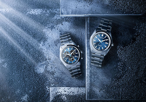 Zwei Citizen-Uhren mit blauen Zifferblättern auf dunklem Textur-Hintergrund.