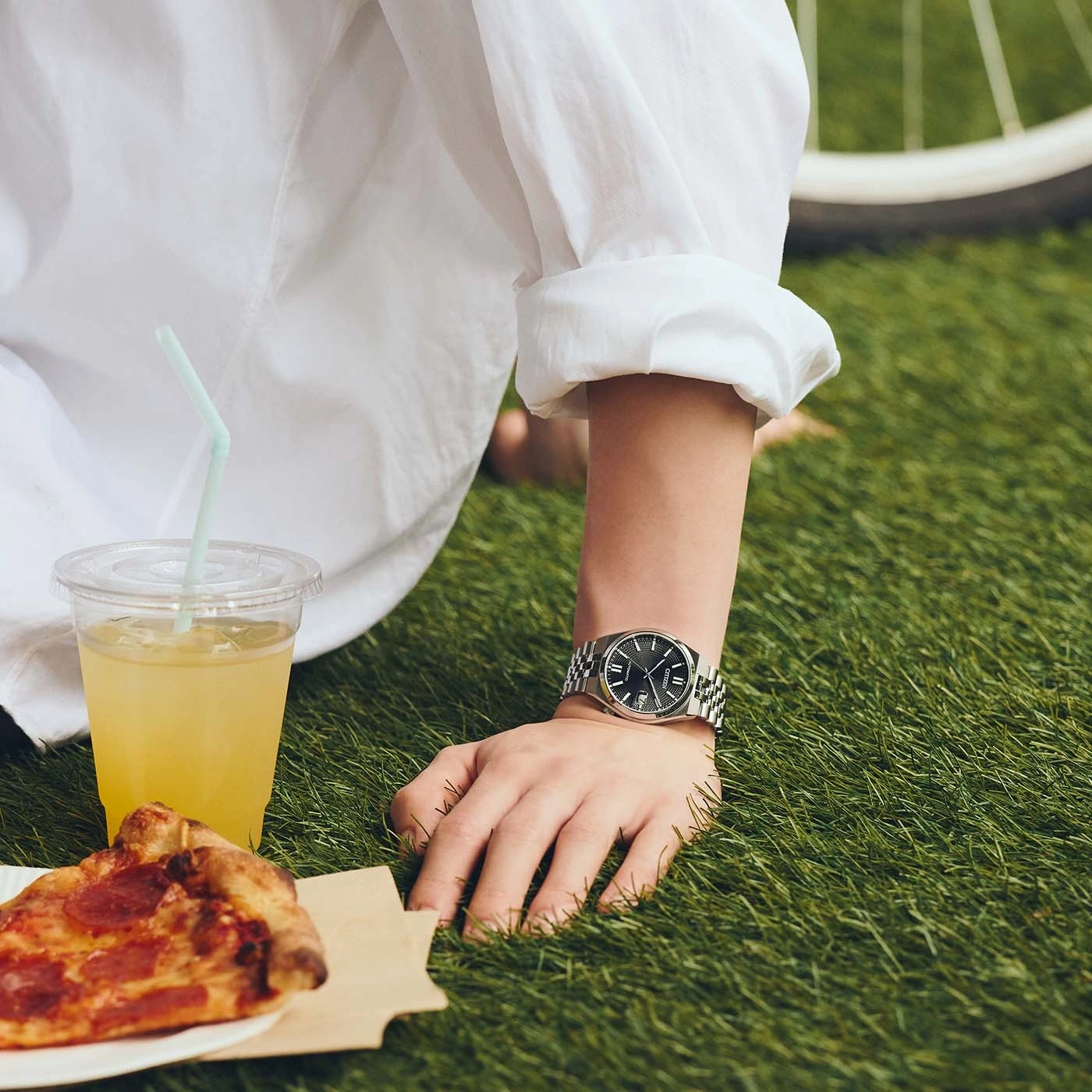 Eine Person in einem weißen Hemd genießt ein Picknick mit Pizza und einem Getränk.