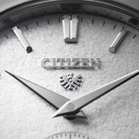 This close-up shows a Citizen watch's brushed silver case, textured white dial, and black leather strap connection.