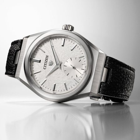 This image features a Citizen watch with a silver-toned case, textured white dial, and black strap, on a reflective surface.