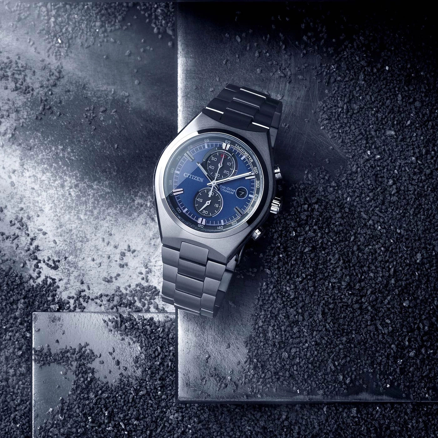 Citizen-Uhr mit blauem Zifferblatt und Titanarmband auf strukturierter Oberfläche.