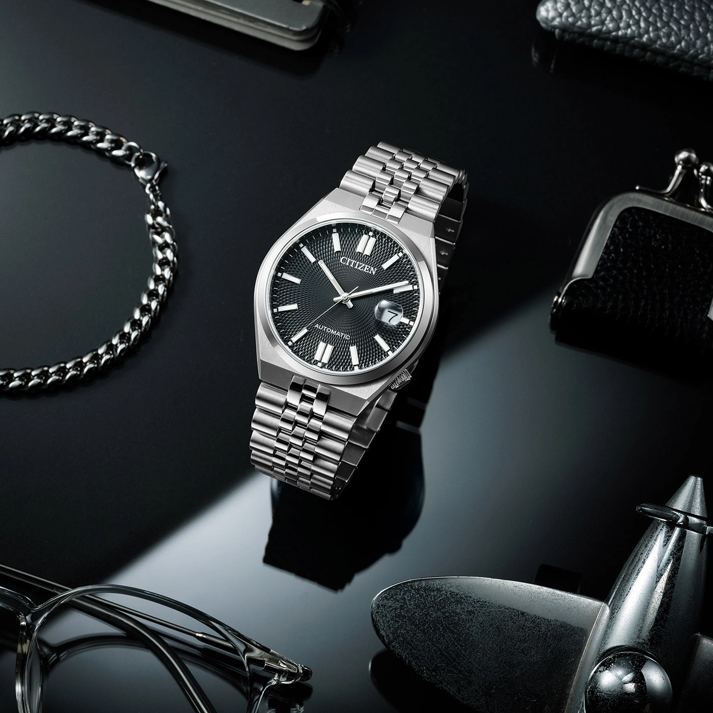 Citizen-Uhr mit Armband, Brille und Accessoires auf schwarzem Untergrund.