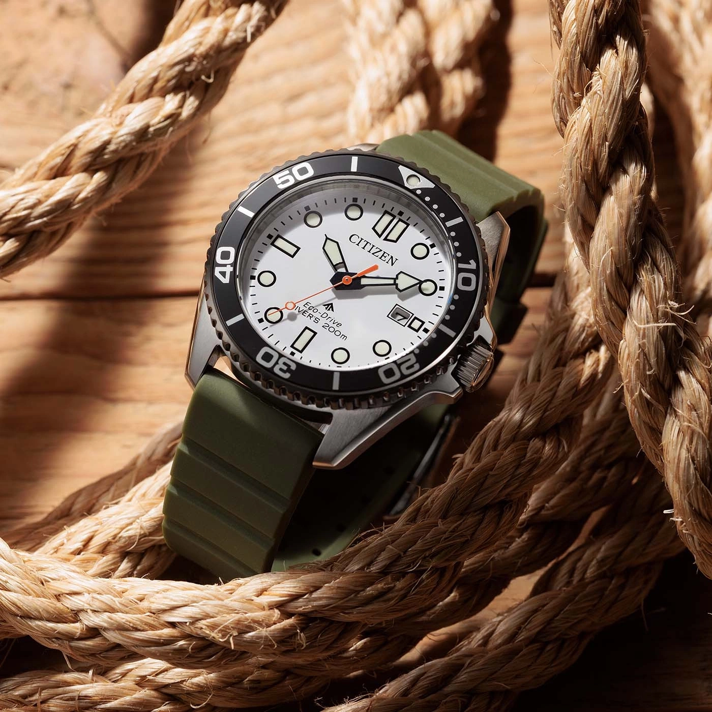 Eine Citizen Eco-Drive Taucheruhr mit weißem Zifferblatt und grünem Band, auf einer Holzoberfläche mit Seil liegend.