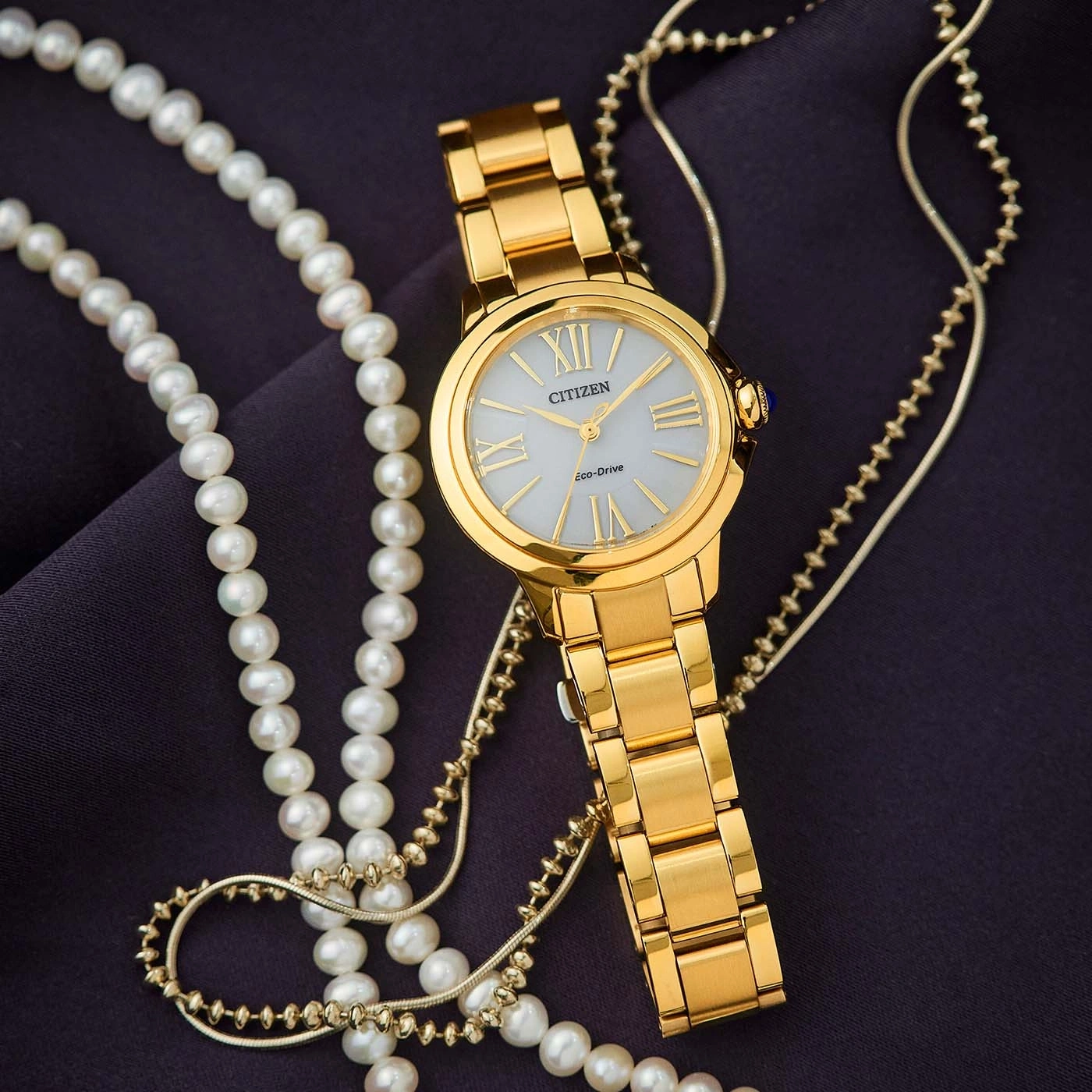 Goldene Uhr mit Perlenkette auf dunklem Stoff