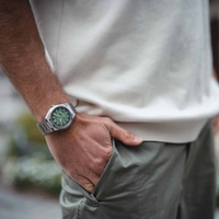Mann trägt silberne Uhr mit grünem Zifferblatt, Hand in der Tasche.