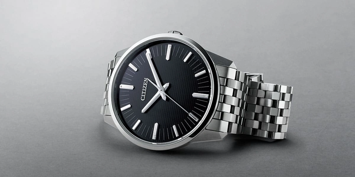 Citizen-Uhr mit schwarzem Zifferblatt und silbernem Armband auf grauem Untergrund
