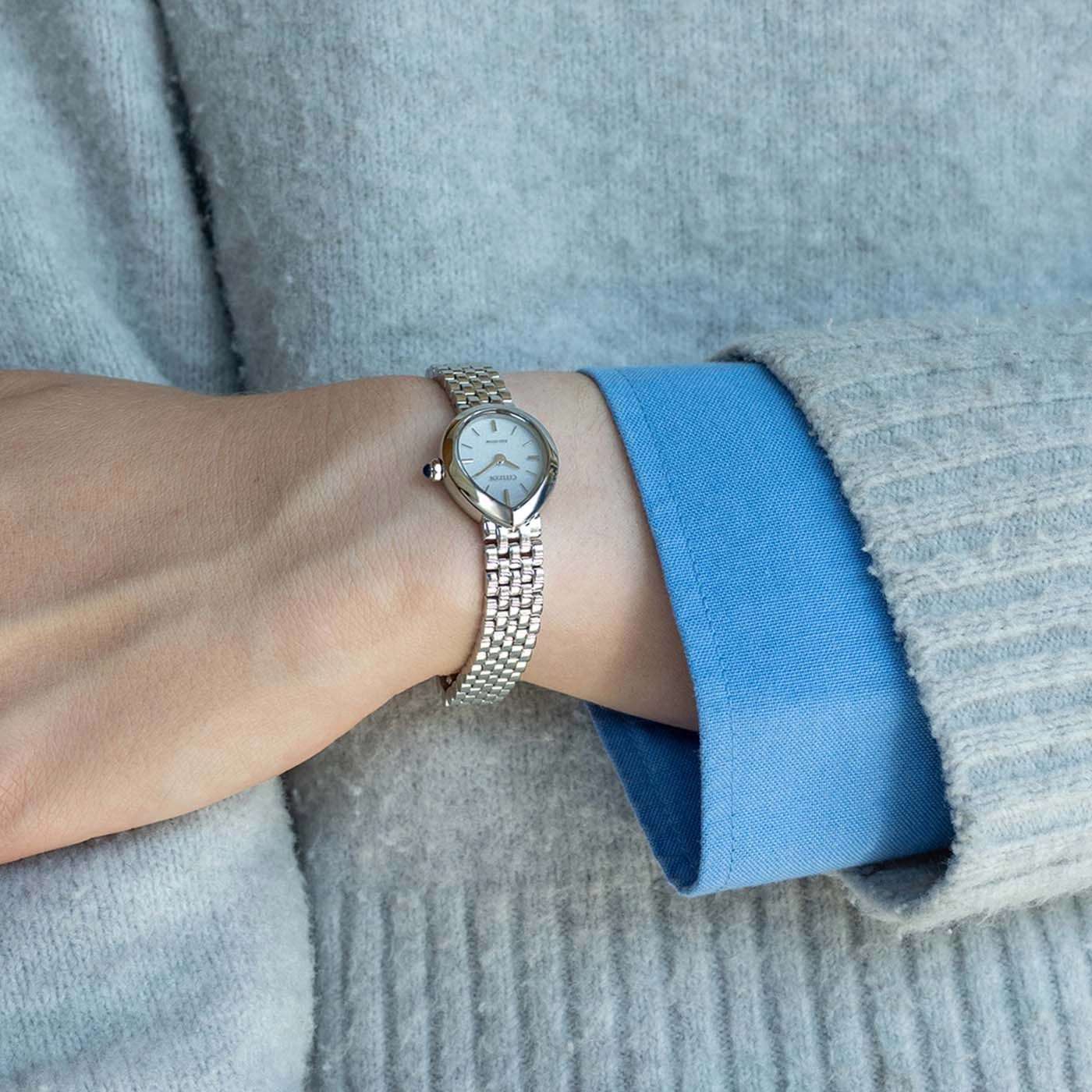 Das Handgelenk einer Frau mit einer silbernen Uhr und einem grauen Pullover.