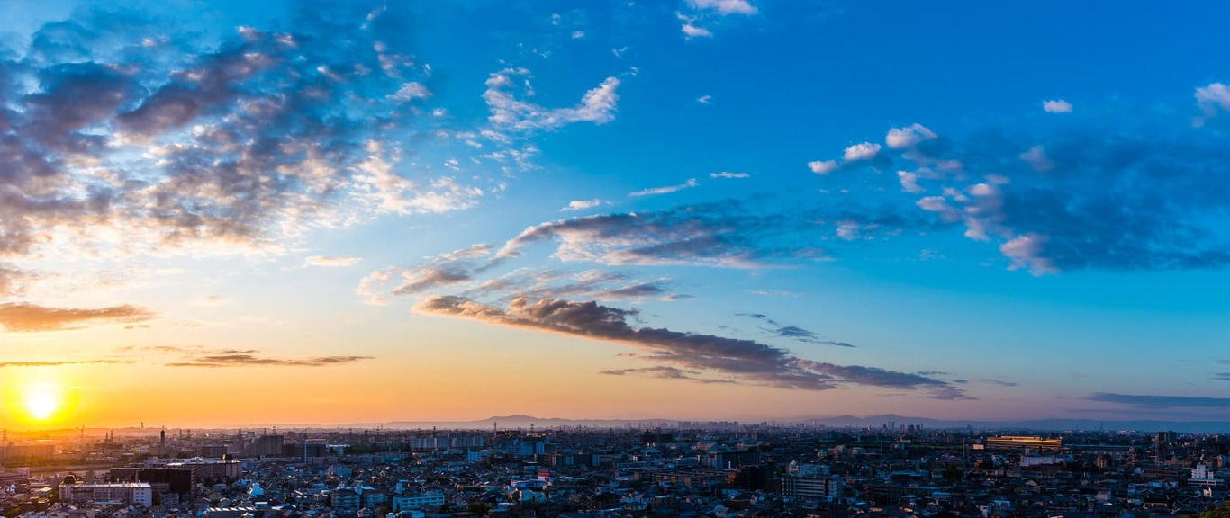 Stadtlandschaft bei Sonnenuntergang mit lebhaftem Himmel und verstreuten Wolken über Gebäuden.