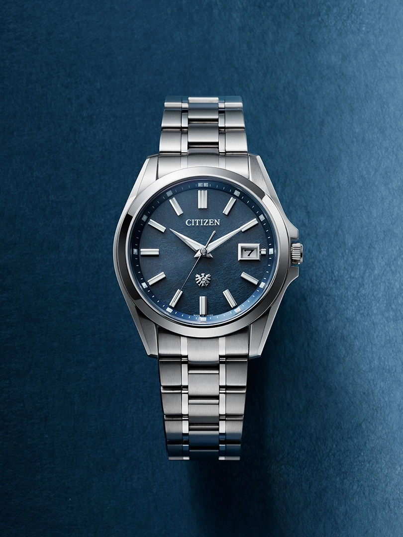 Citizen-Uhr mit blauem Zifferblatt und silbernem Armband auf blauem Hintergrund.