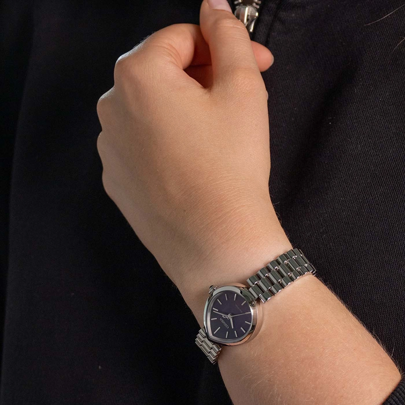 Eine Frauenhand trägt eine silberne Uhr mit dunklem Zifferblatt.