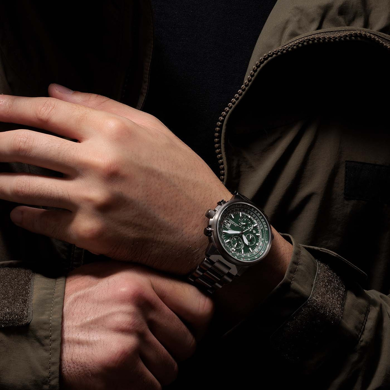 Mann mit grüner Uhr, verschränkte Hände, dunkle Jacke, Nahaufnahme.