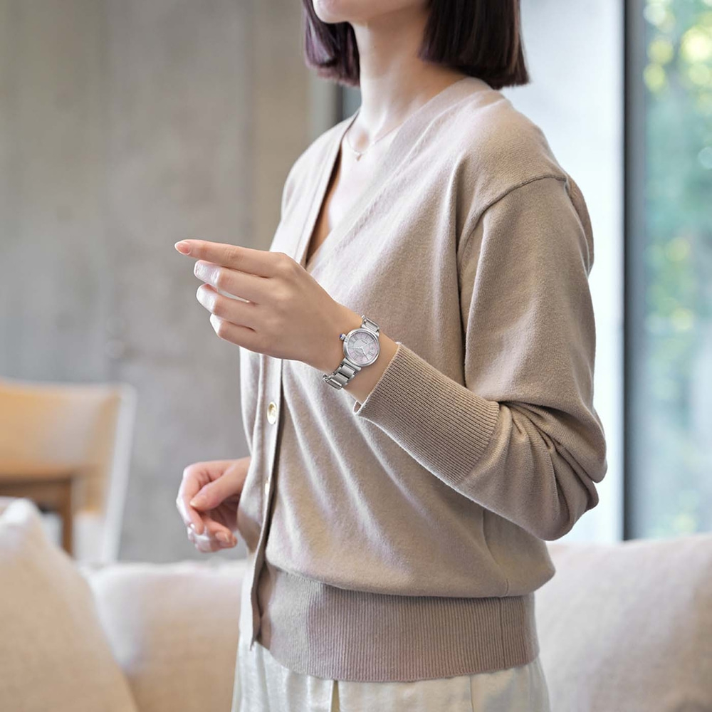 Frau trägt eine beige Strickjacke und eine silberne Uhr, die zeigt.