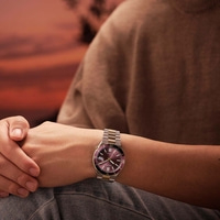 Mann trägt eine Uhr mit lila Zifferblatt und Metallarmband.