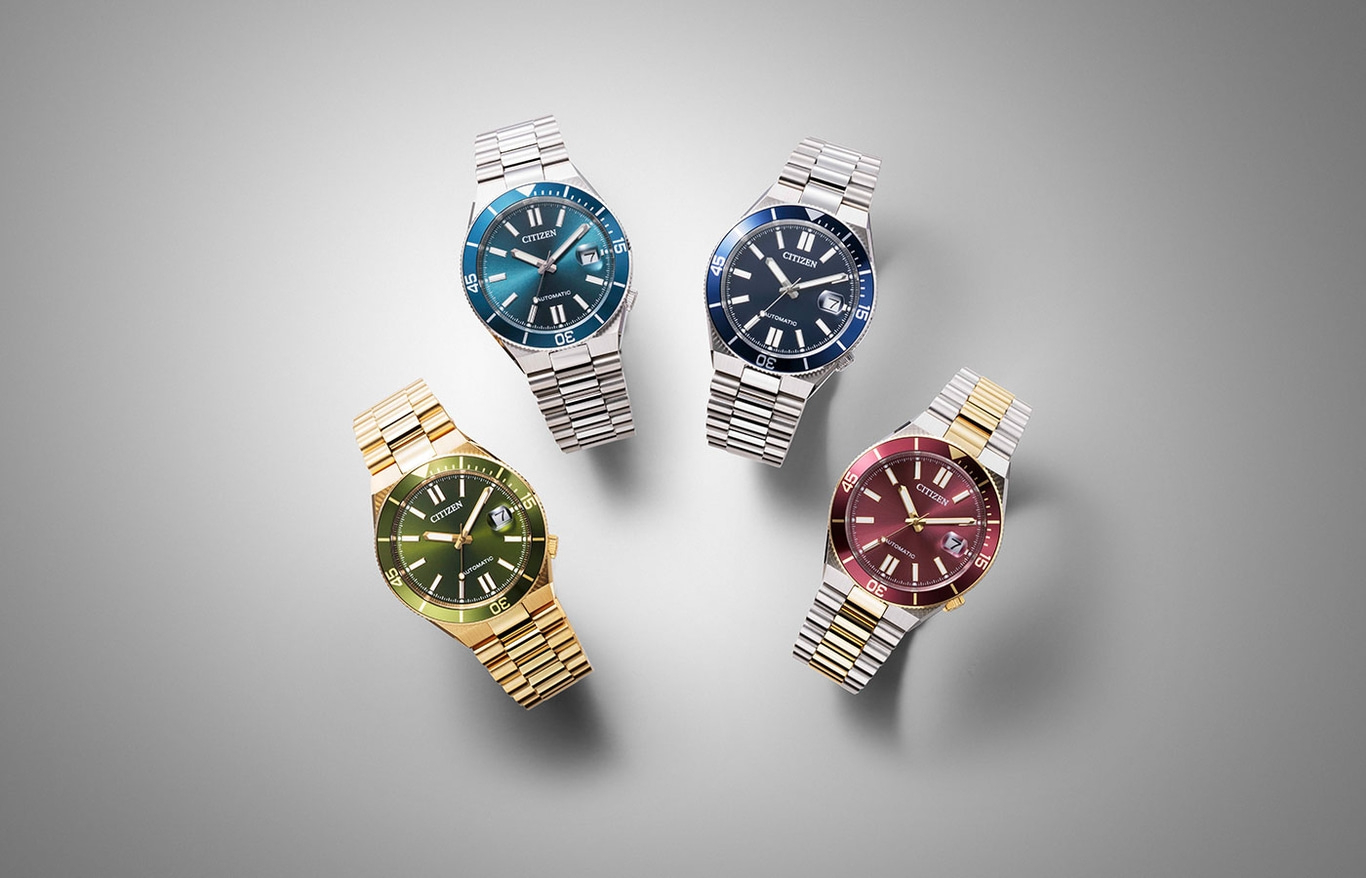 Vier Citizen-Uhren mit verschiedenfarbigen Zifferblättern auf grauem Hintergrund.