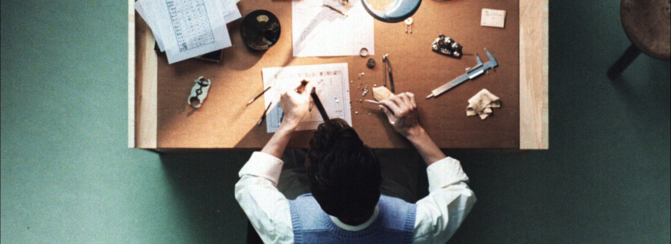 Eine Person arbeitet an einem Tisch mit Werkzeugen und Papieren, Draufsicht.