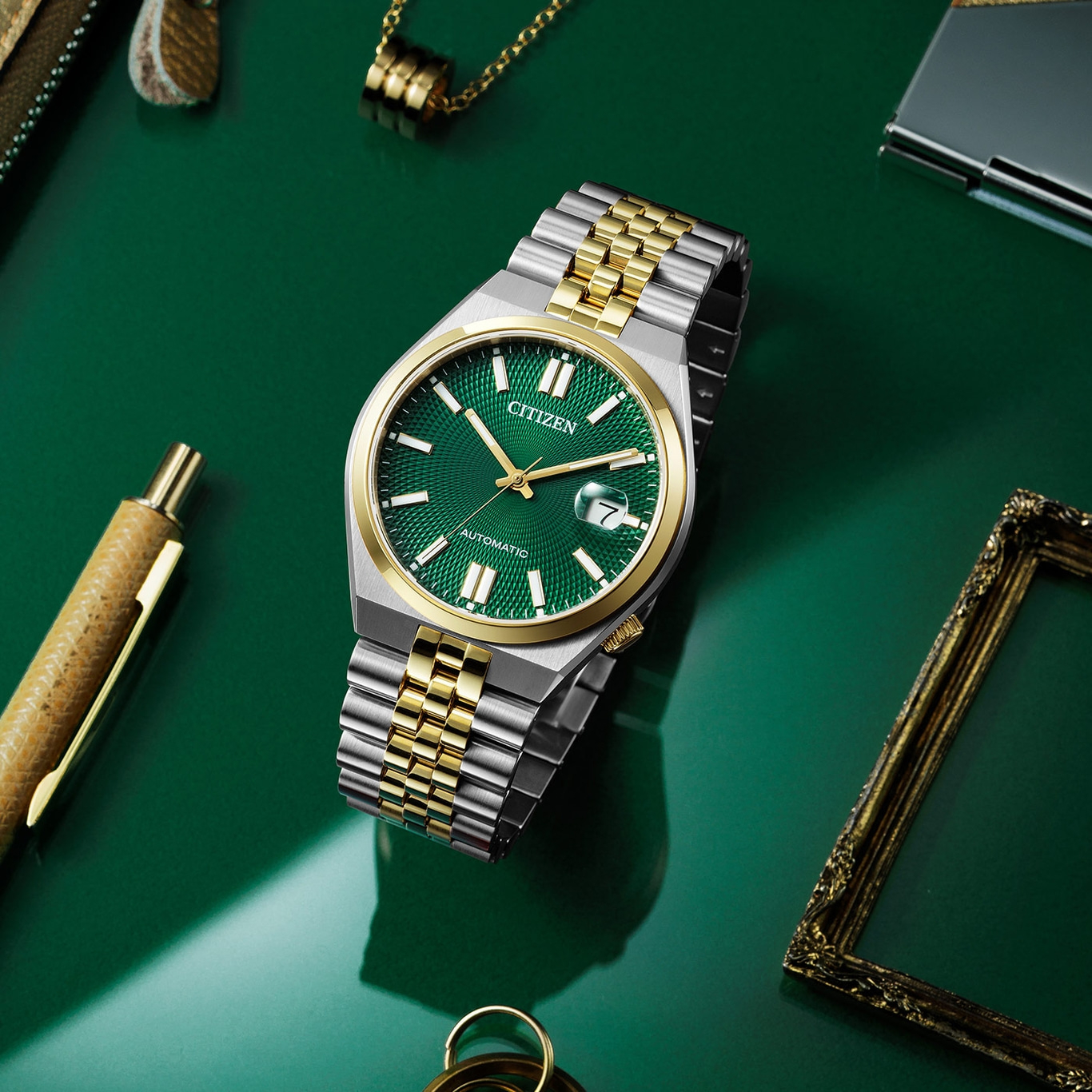 Citizen-Uhr mit grünem Zifferblatt und goldenen Akzenten auf grünem Untergrund.