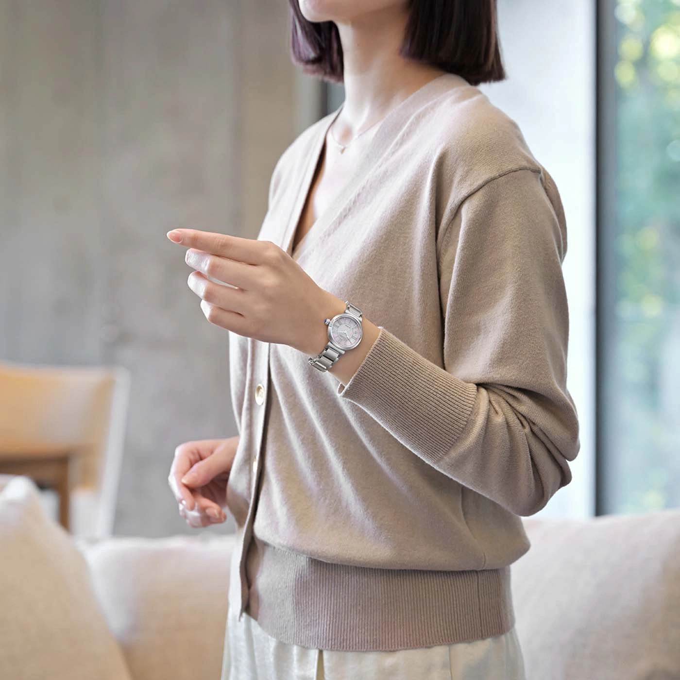 Frau trägt eine beige Strickjacke und eine silberne Uhr, die zeigt.