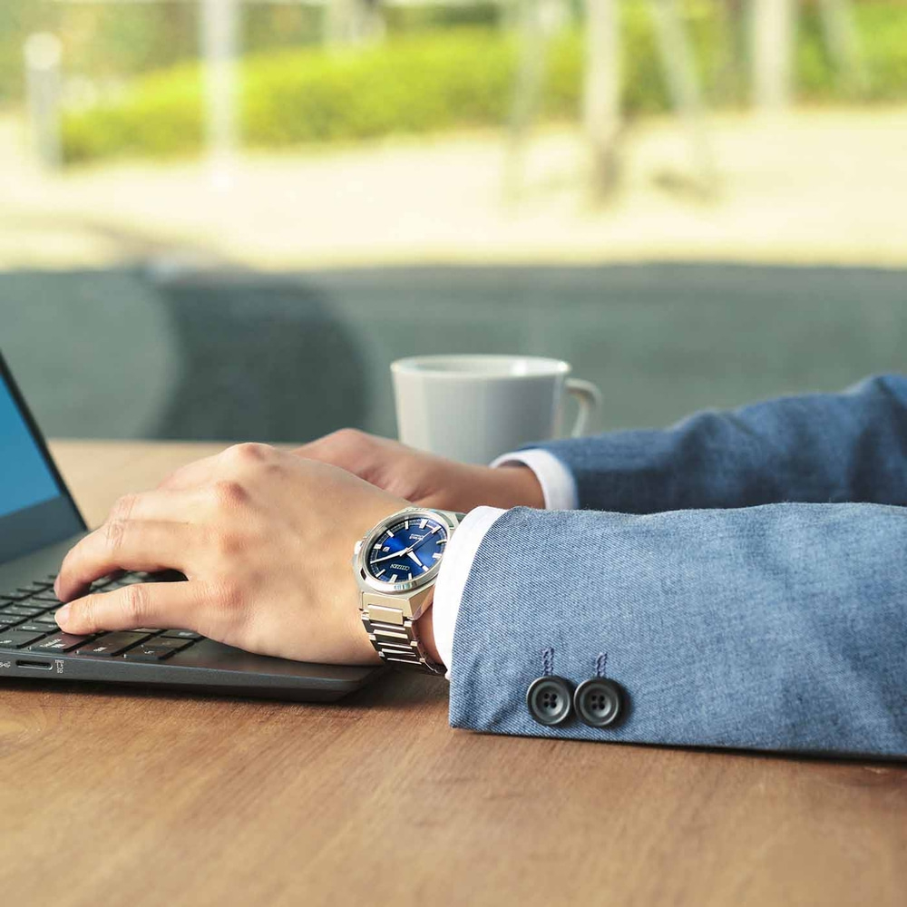 Mann mit Uhr, tippt auf Laptop, mit einer Tasse Kaffee auf dem Tisch.