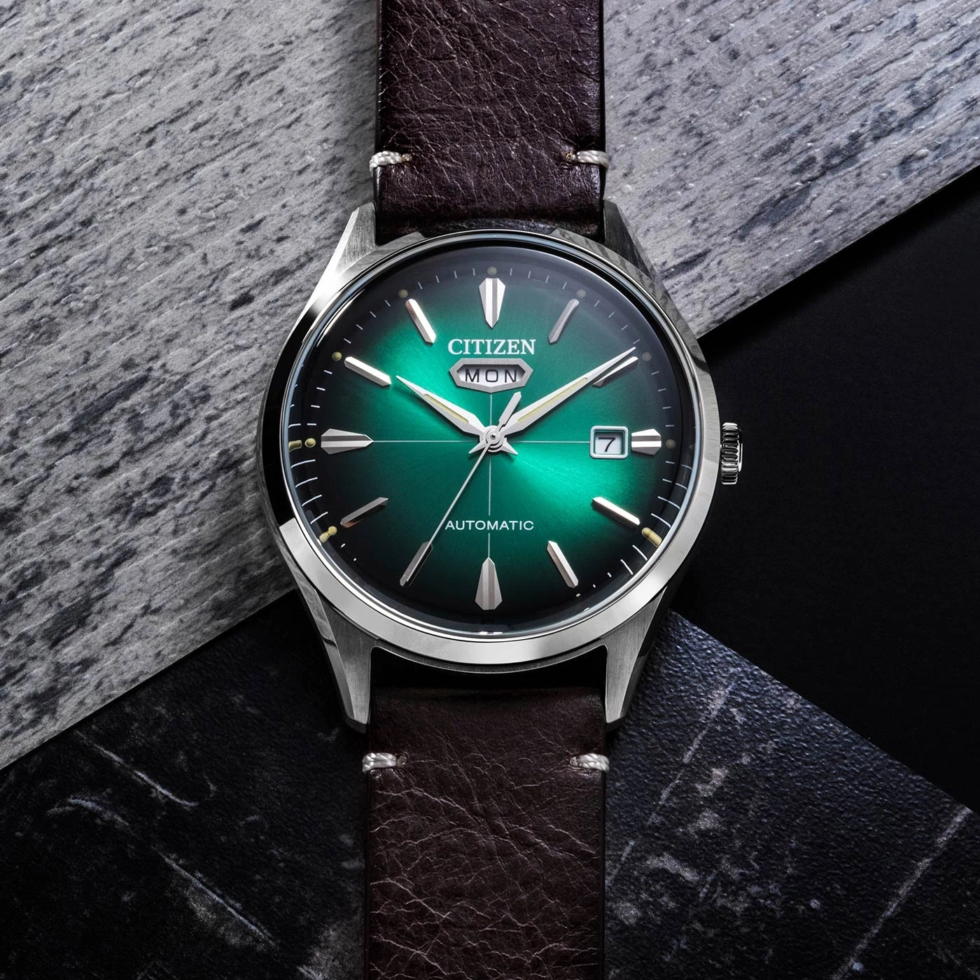 Citizen-Uhr mit grünem Zifferblatt und braunem Lederarmband auf strukturierter Oberfläche.