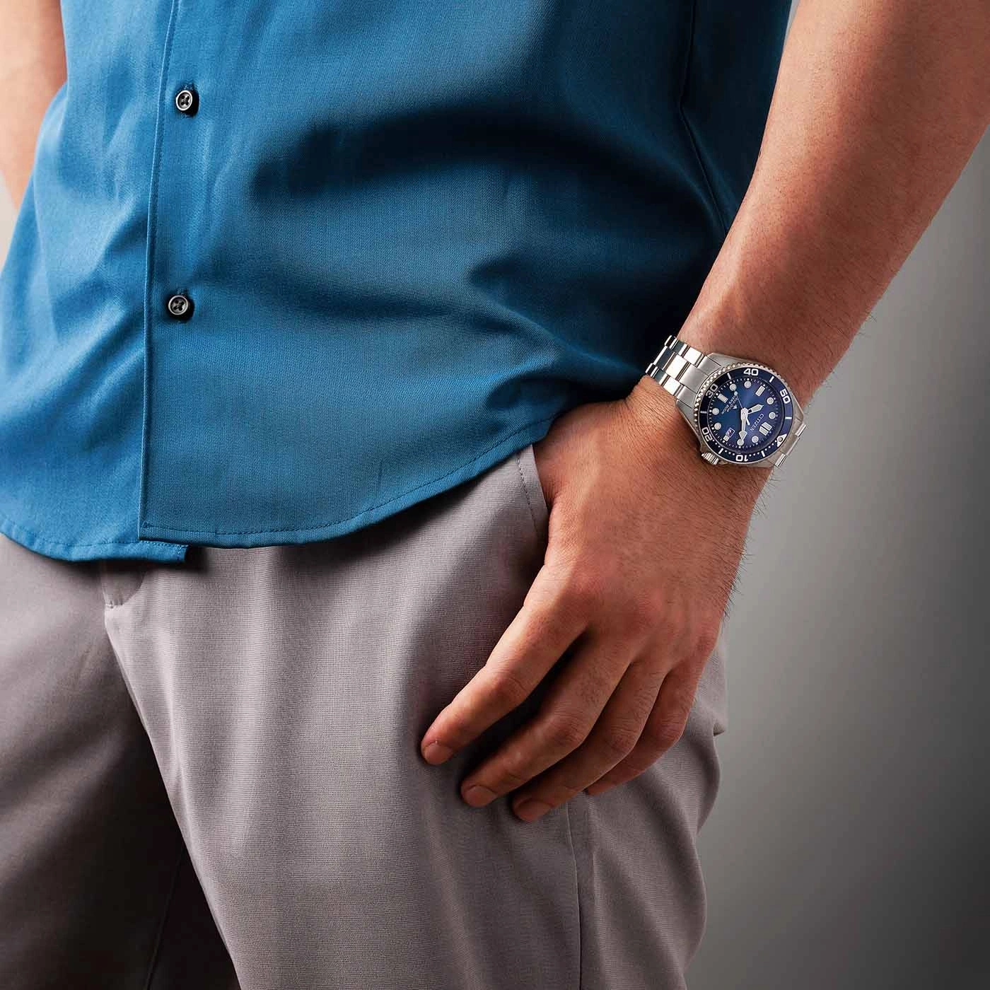 Mann mit blauem Hemd und grauer Hose, der eine Uhr am Handgelenk trägt.