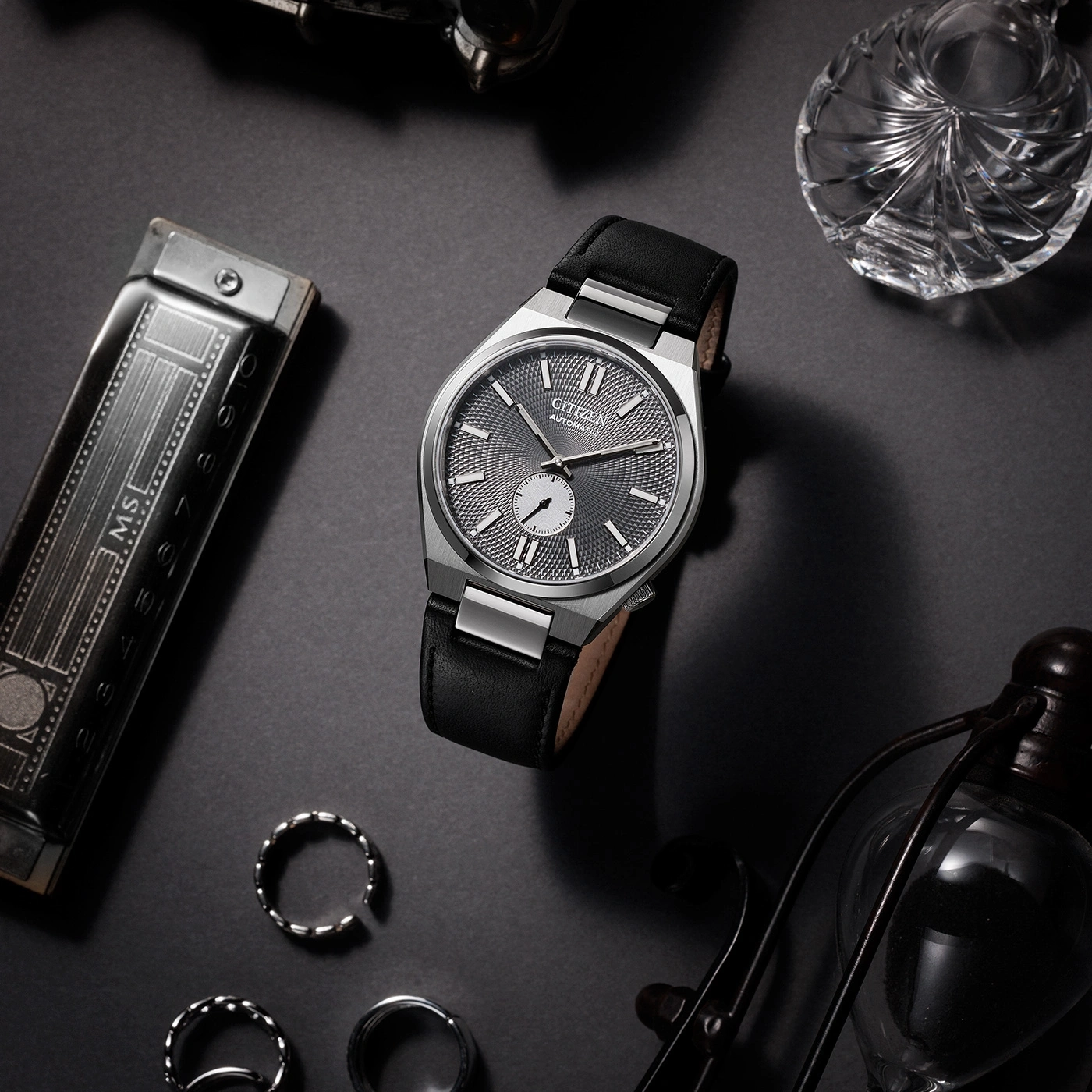 Citizen-Uhr mit schwarzem Lederarmband und Zubehör auf dunkler Oberfläche.