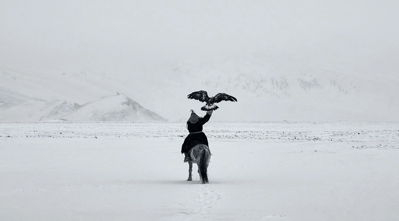 Mann auf Pferd mit Adler in schneebedeckter Landschaft, monochrom.