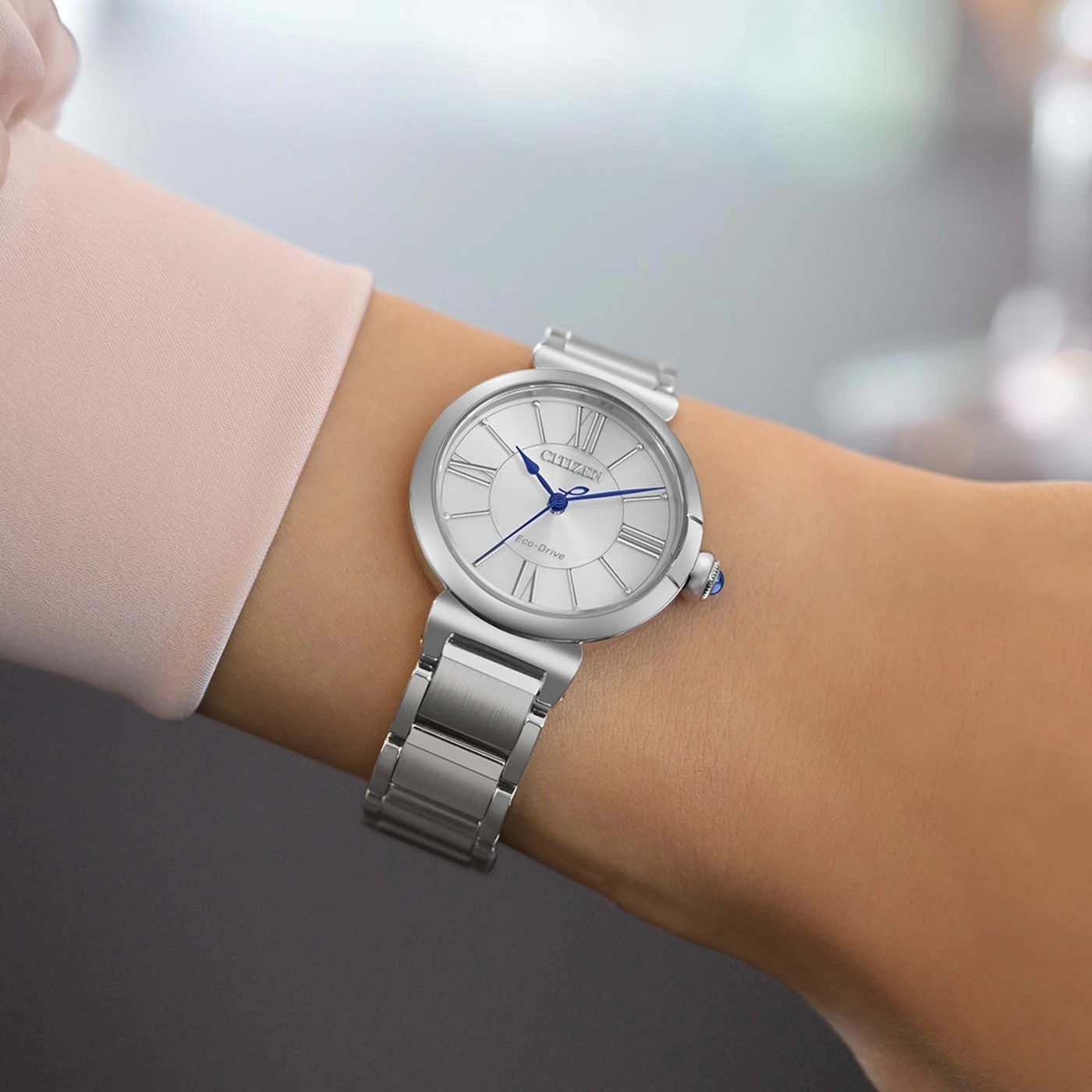 Eine Frau trägt eine silberne Citizen Eco-Drive Uhr mit römischem Zifferblatt.
