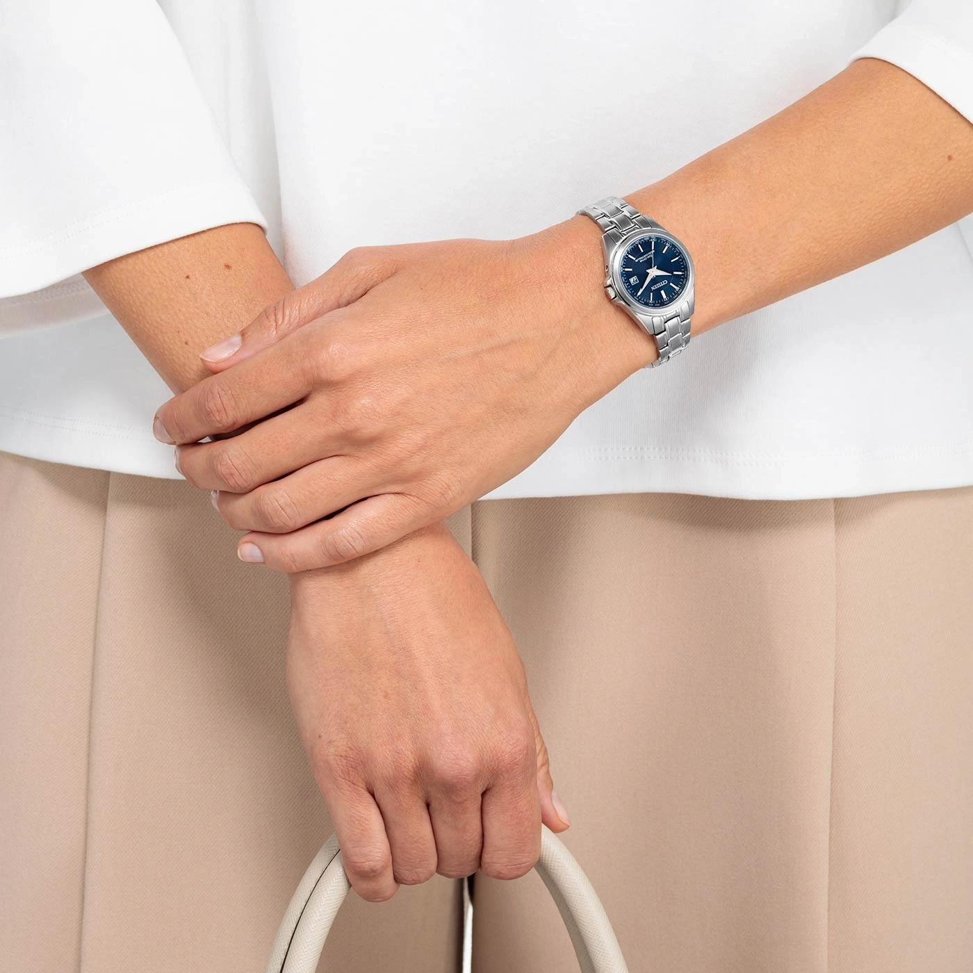Frau mit Uhr, Handtasche, weißem Hemd und beiger Hose.