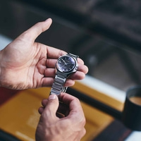 Nahaufnahme einer Person, die eine Citizen-Uhr mit schwarzem Zifferblatt hält.