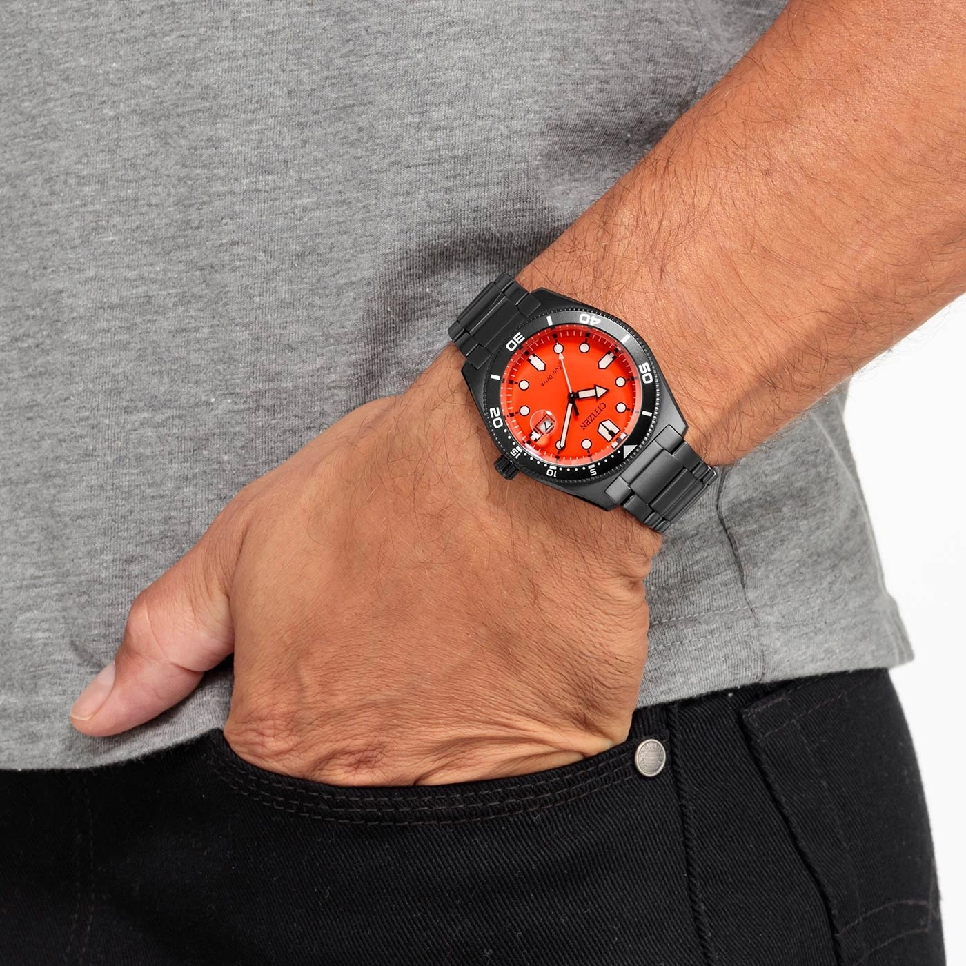 Mann mit schwarzer Uhr mit orangefarbenem Zifferblatt, grauem Hemd und schwarzer Hose.