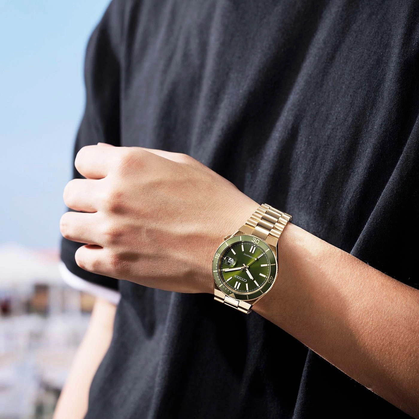 Mann trägt eine goldene Citizen-Uhr mit grünem Zifferblatt.
