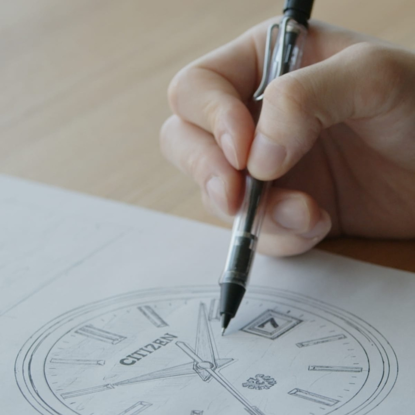 Hand zeichnet mit einem Stift ein Citizen-Uhrendesign auf Papier.