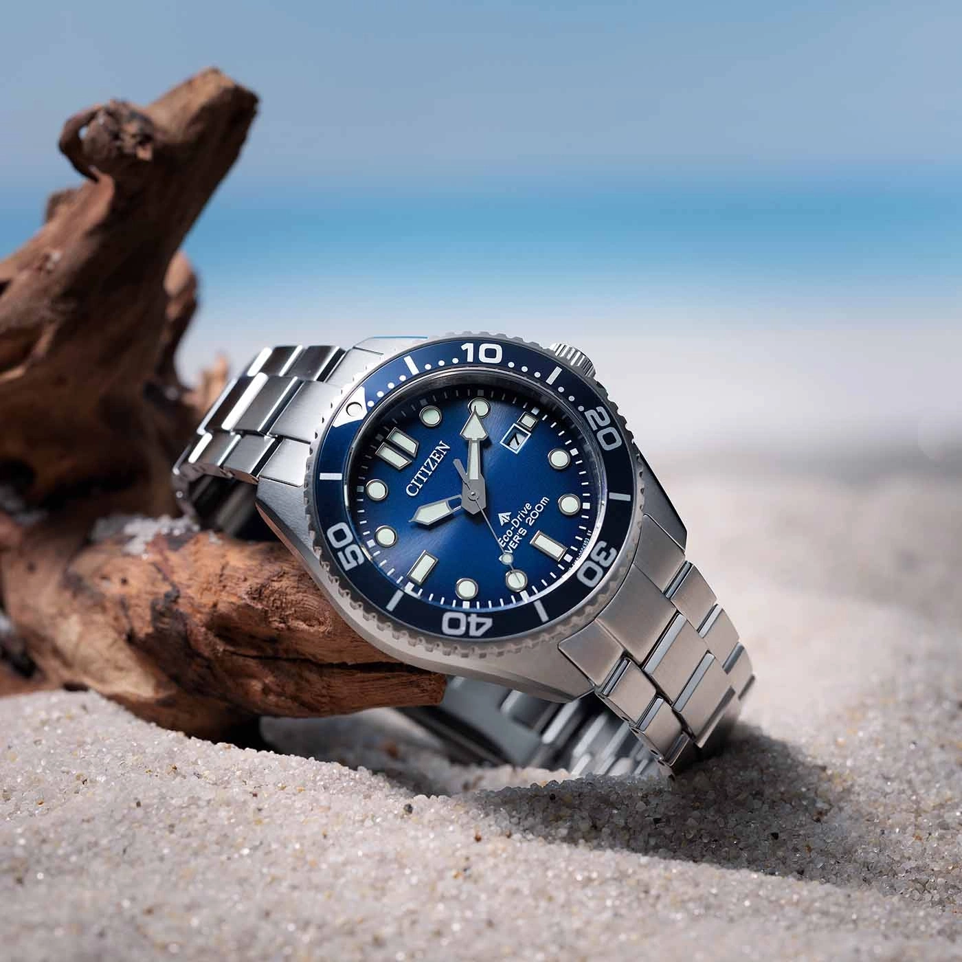 Citizen-Uhr auf Sand mit blauem Zifferblatt und Ozeanhintergrund