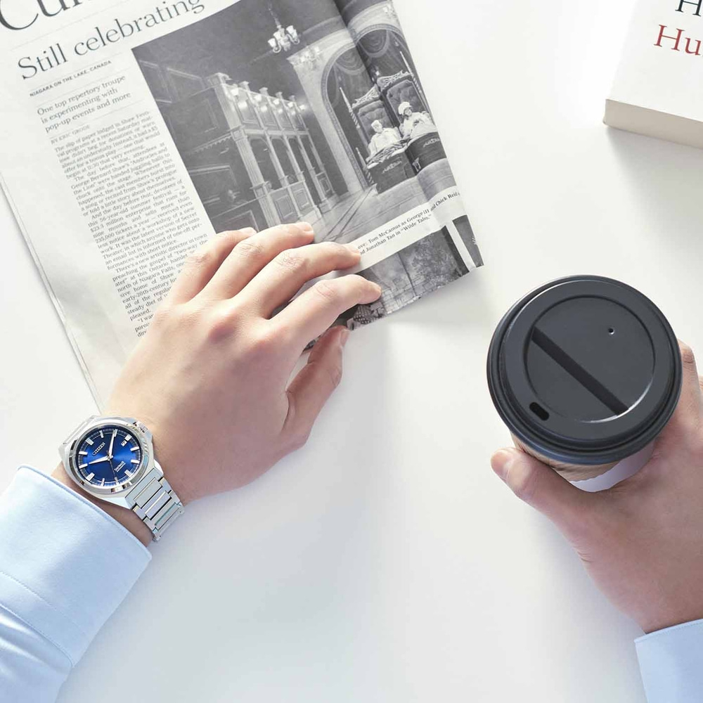 Mann hält Zeitung und Kaffee, trägt eine Uhr.