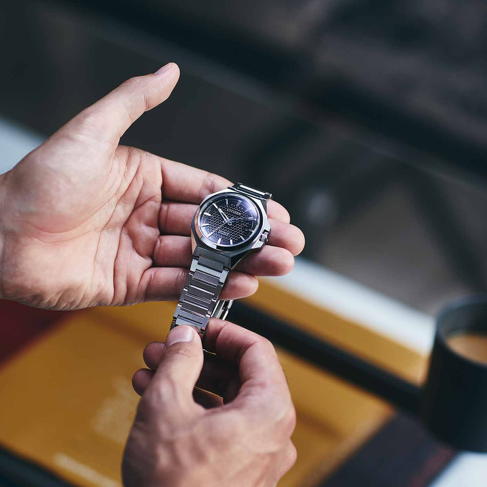 Nahaufnahme einer Person, die eine Citizen-Uhr mit schwarzem Zifferblatt hält.