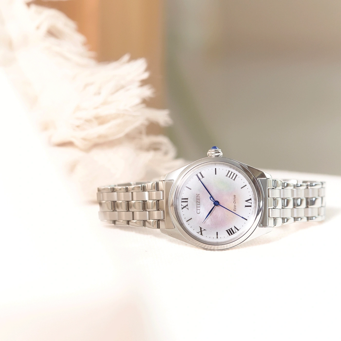 Citizen-Uhr mit weißem Zifferblatt und silbernem Armband auf weißer Oberfläche.