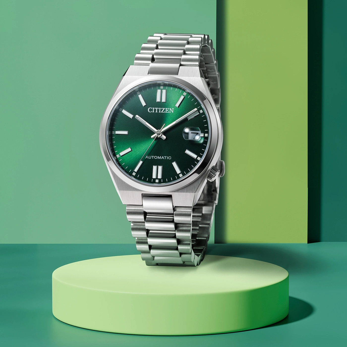 Citizen-Uhr mit grünem Zifferblatt und silbernem Armband auf grüner Plattform.