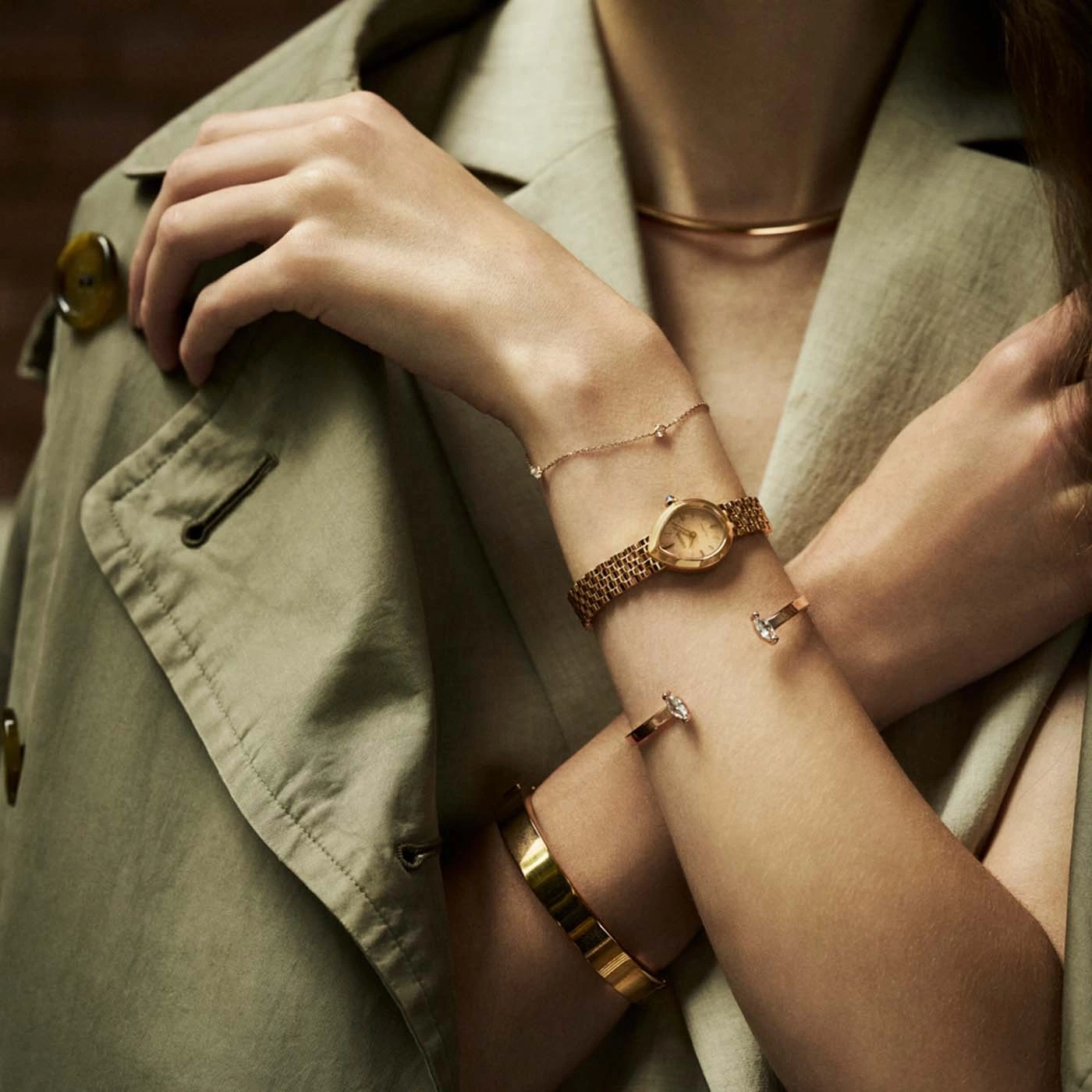 Nahaufnahme der Arme einer Frau mit goldenem Schmuck, einschließlich einer Uhr und Armbändern.