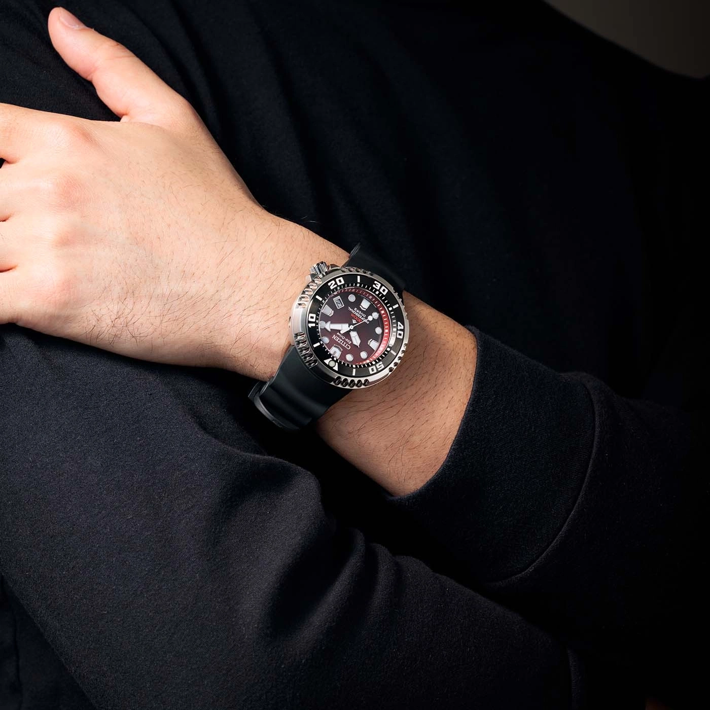 Mann trägt Citizen-Uhr mit schwarzem Armband und rotem Zifferblatt.