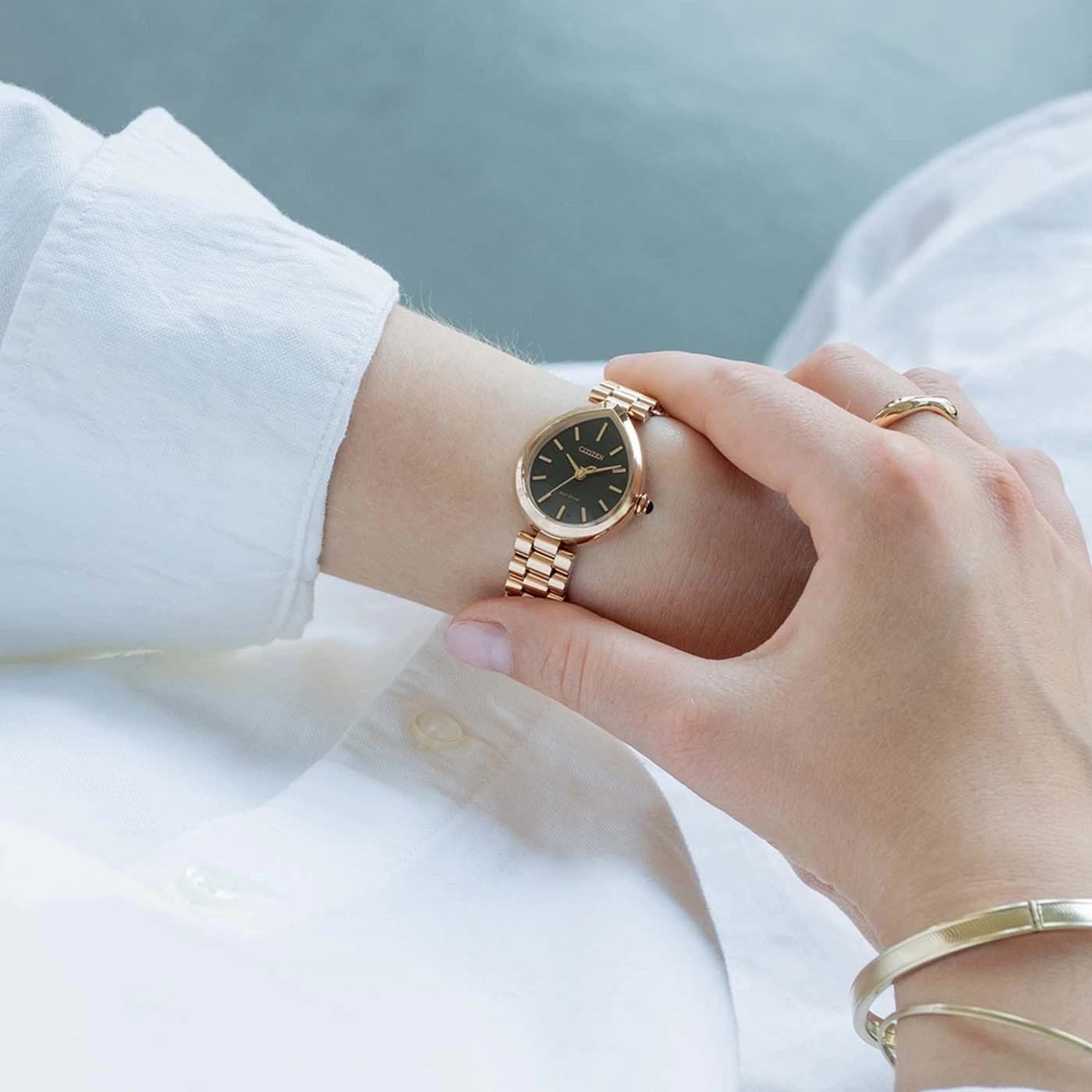 Eine Frau trägt eine goldene Uhr und ein Armband und berührt ihr Gesicht.