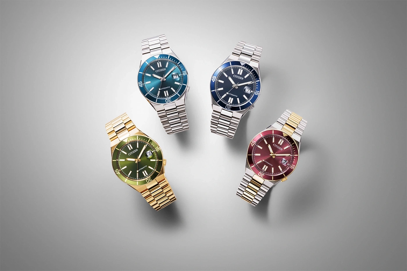 Vier Citizen-Uhren mit unterschiedlich farbigen Zifferblättern und Metallarmbändern auf grauem Hintergrund.