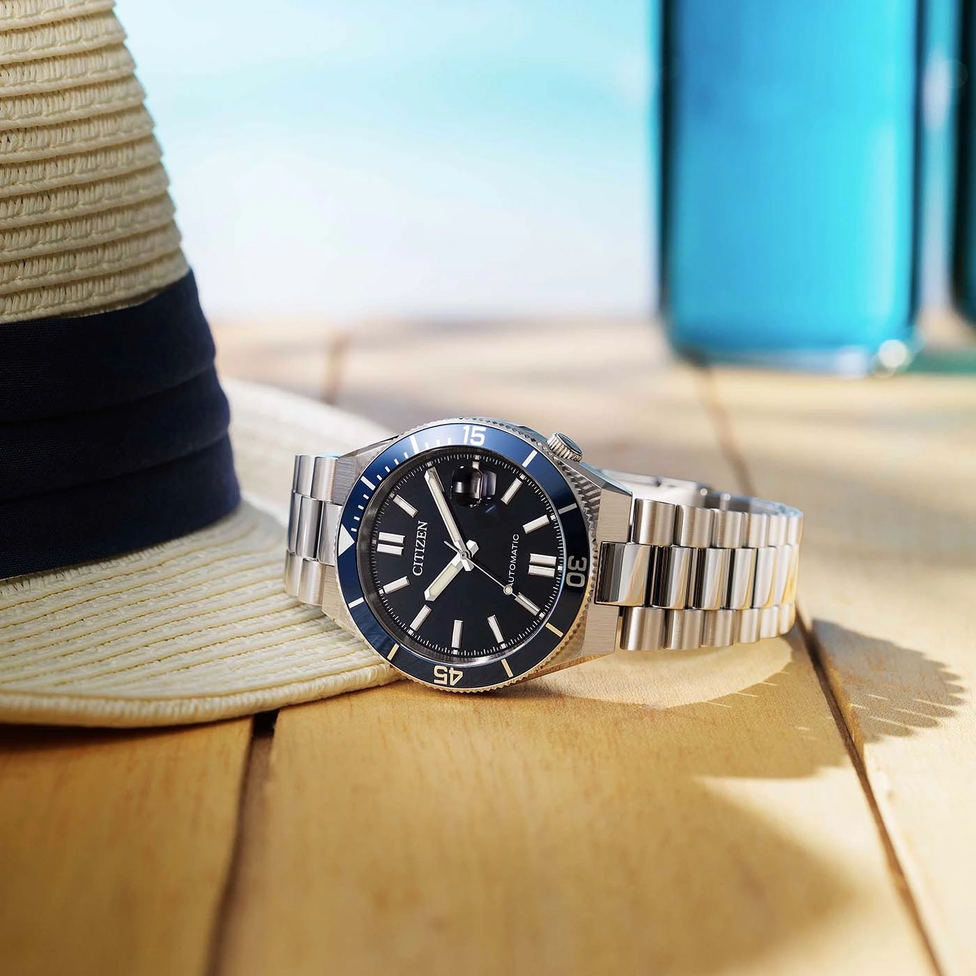 Eine Citizen-Uhr auf einem Holztisch mit Hut und Getränken.