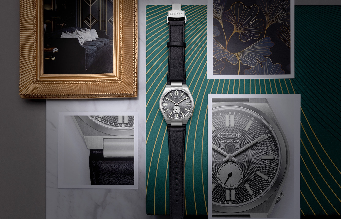 Citizen-Uhr mit schwarzem Lederarmband auf grünem Hintergrund mit goldenen Akzenten.