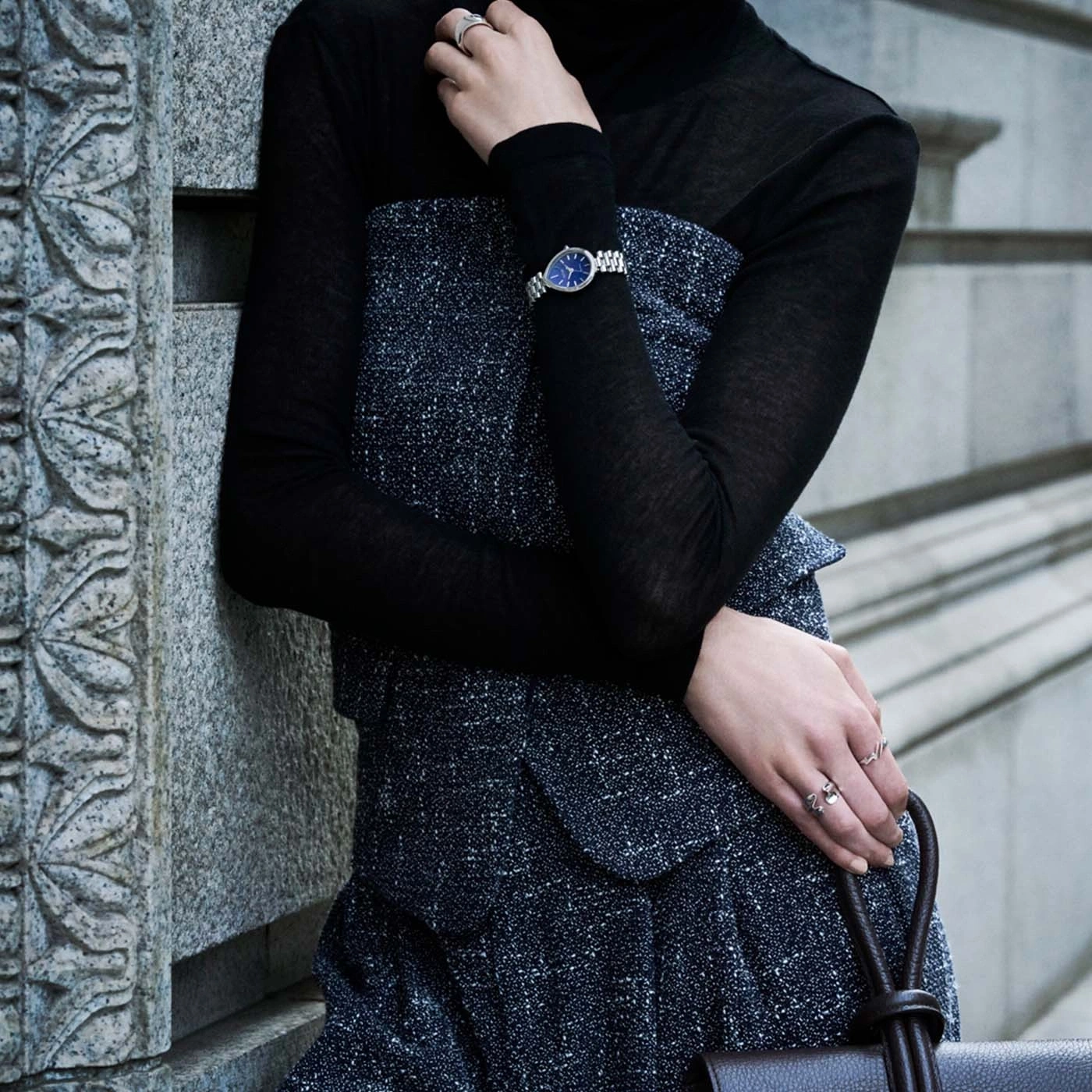 Frau im schwarzen Rollkragenpullover und gemustertem Kleid mit Uhr und Ringen.