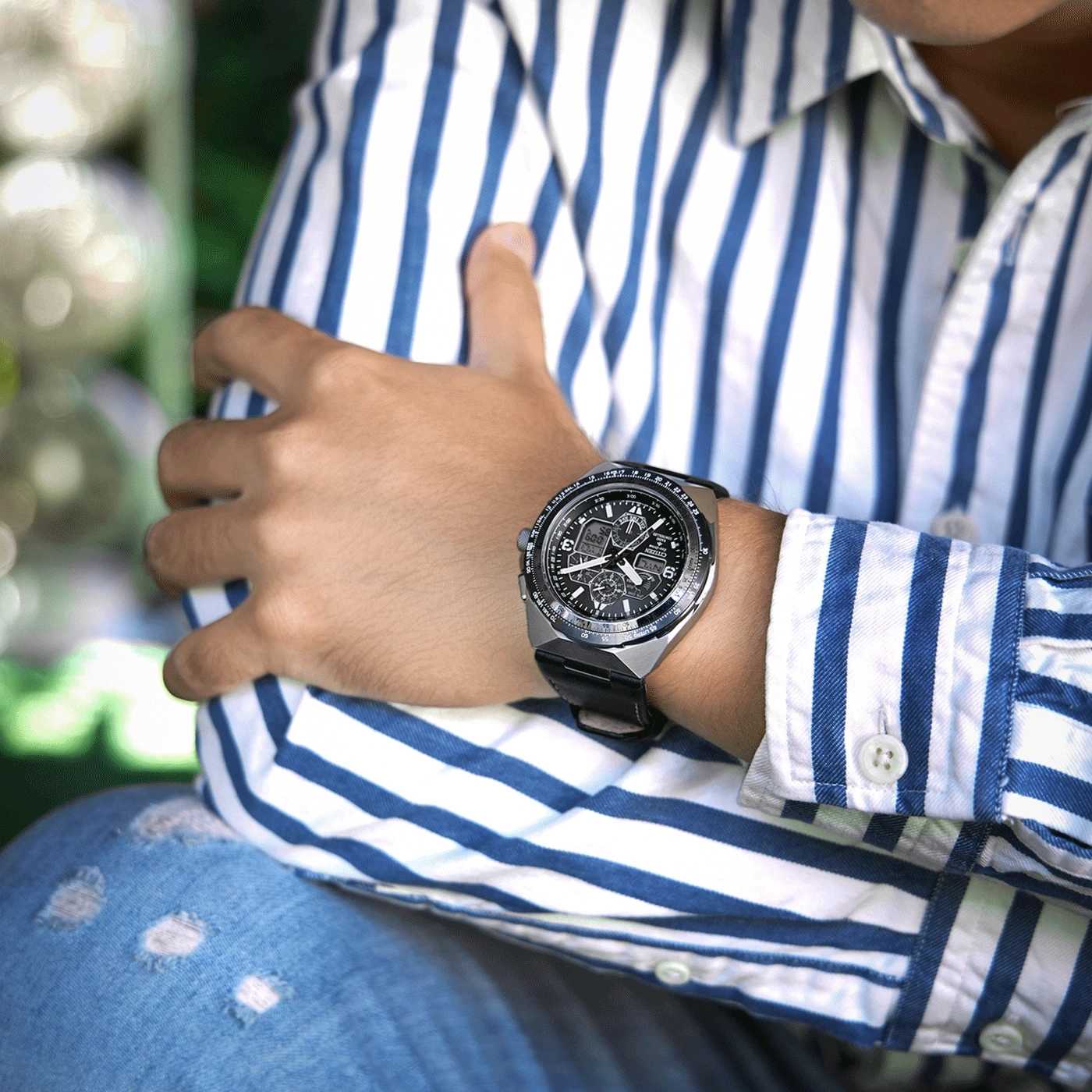 Mann mit Uhr, blau-weiß gestreiftem Hemd und zerrissener Jeans.
