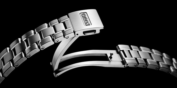 This close-up features a polished metal watch bracelet with a visible 'CITIZEN' logo on its clasp. The intricate links and release mechanism are sharply detailed against a dark background, highlighting the quality and craftsmanship of the watch band.