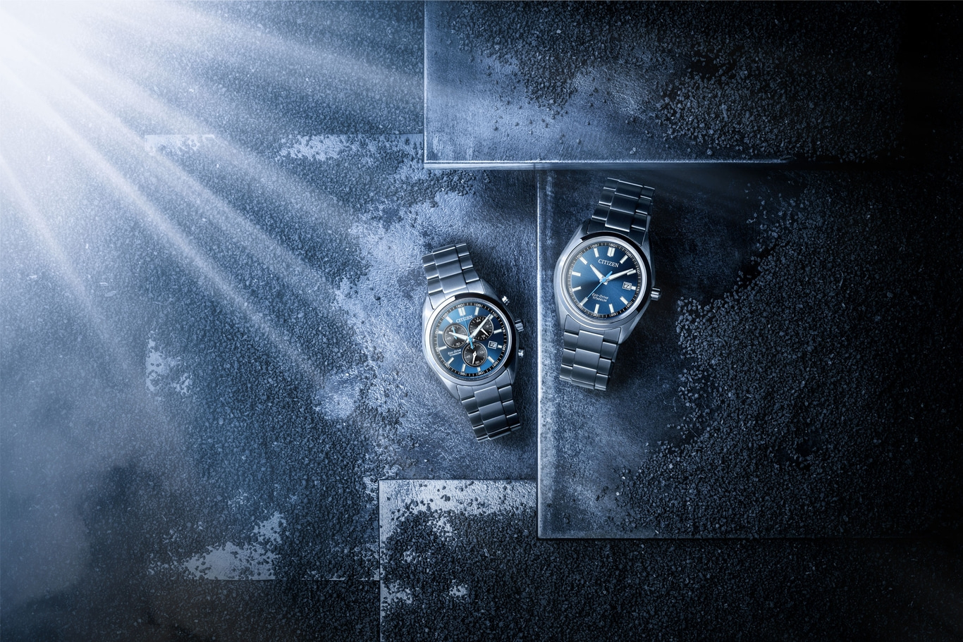 Zwei Citizen Eco-Drive Titanuhren auf dunkler Strukturfläche mit Lichtstrahlen.