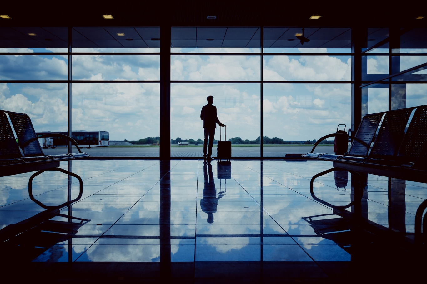 Silhouette einer Person mit Gepäck in einem Flughafen, die aus dem Fenster schaut.