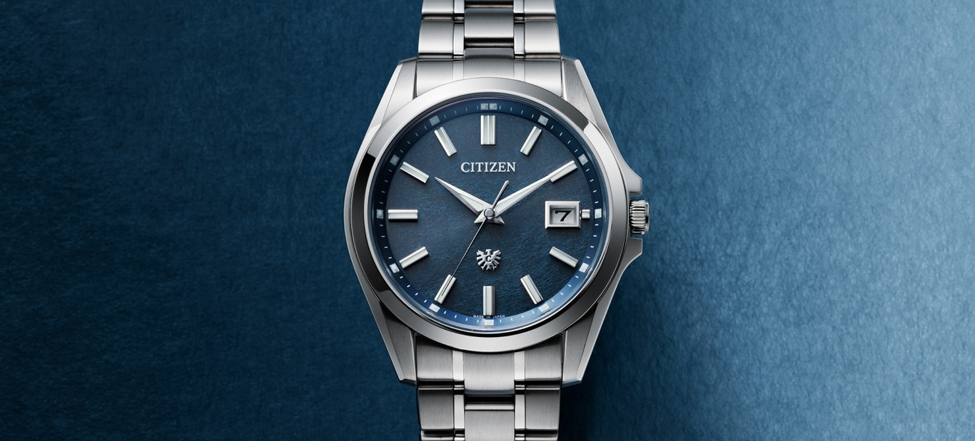This image features a sophisticated Citizen Eco-Drive watch with a deep blue dial and a polished silver-toned case and integrated bracelet. It has applied hour markers, a date window, and a refined design, set against a subtly textured blue background.