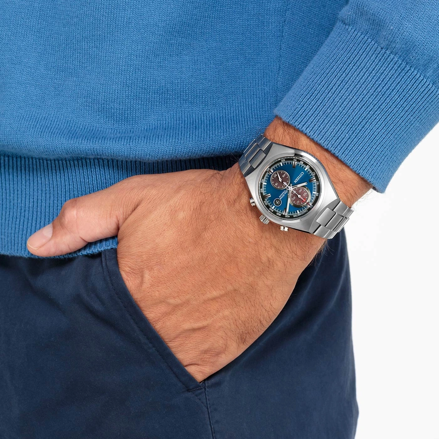 Mann mit blauer Uhr, blauem Pullover und blauer Hose, Hand in der Tasche.